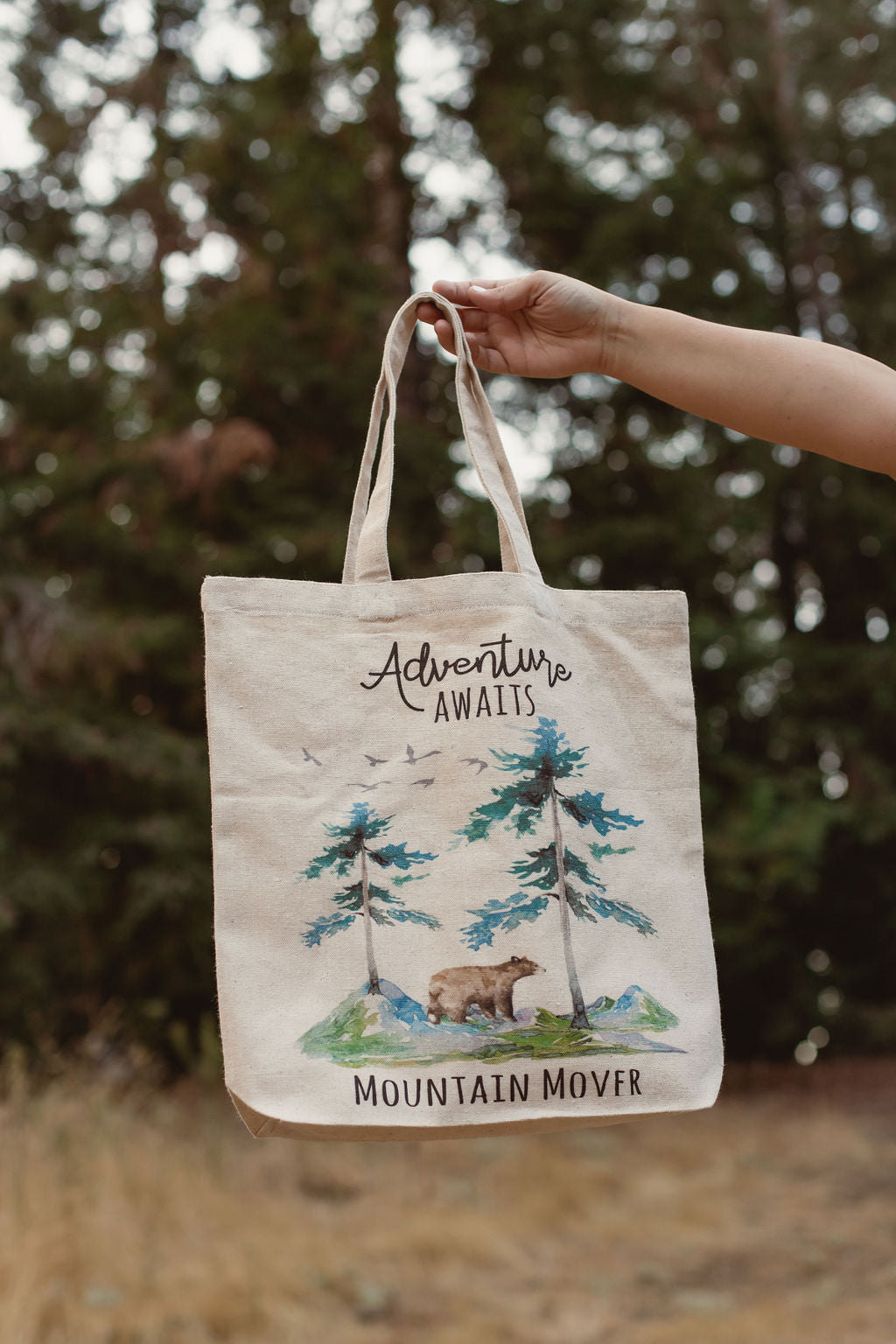 white canvas bag that says adventure awaits with bear and mountain scene