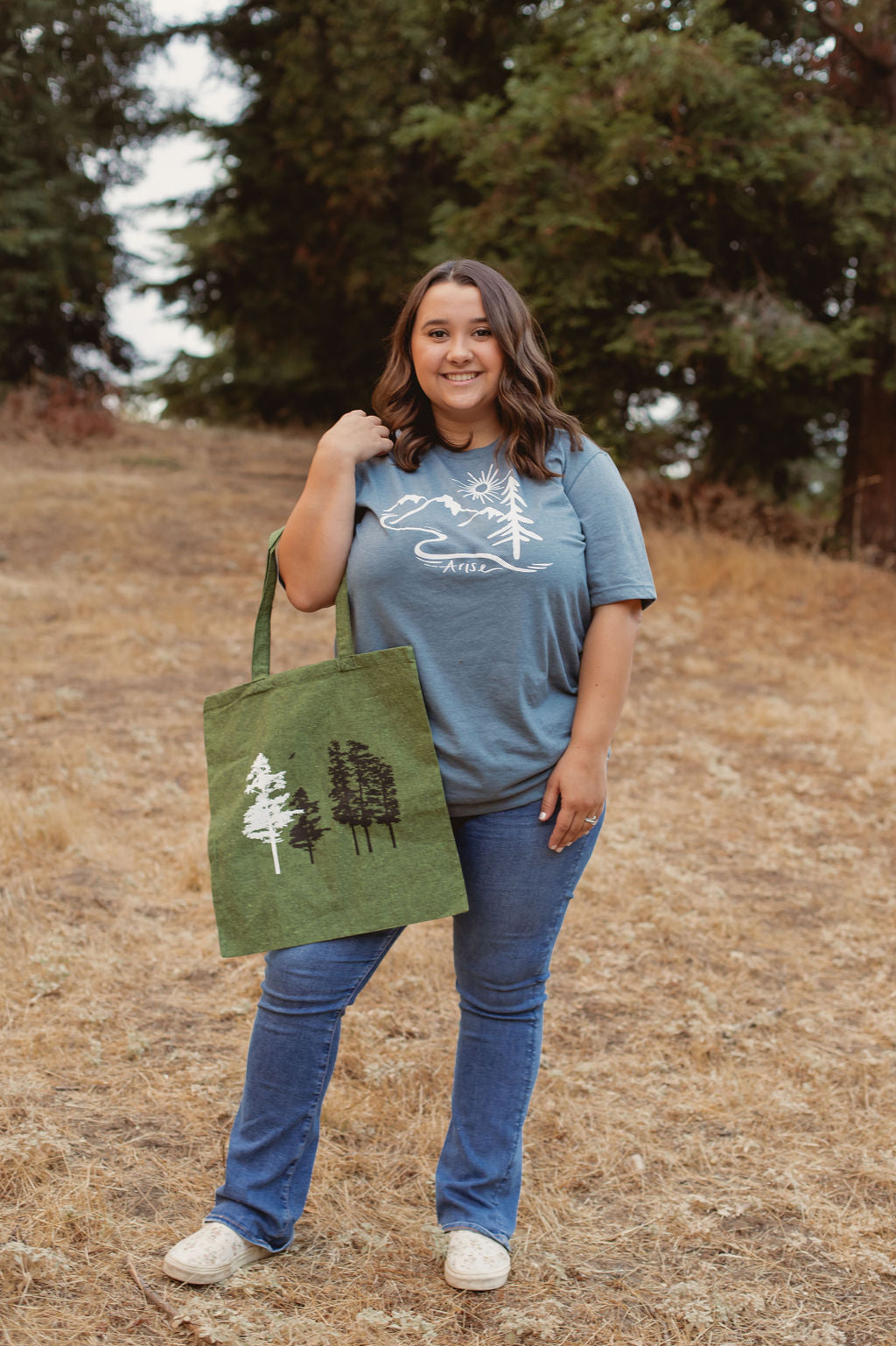 Woman in Arise T-shirt with dark green canvas bag with white and black tree stamps