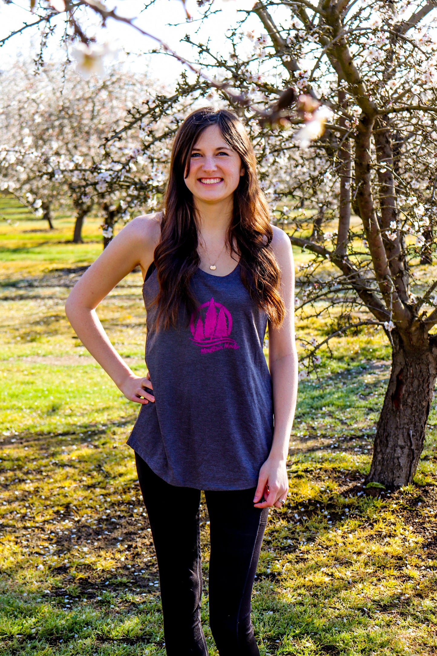 Woman wearing gray tank top with pink stamp showing three trees with mountain mover text beneath