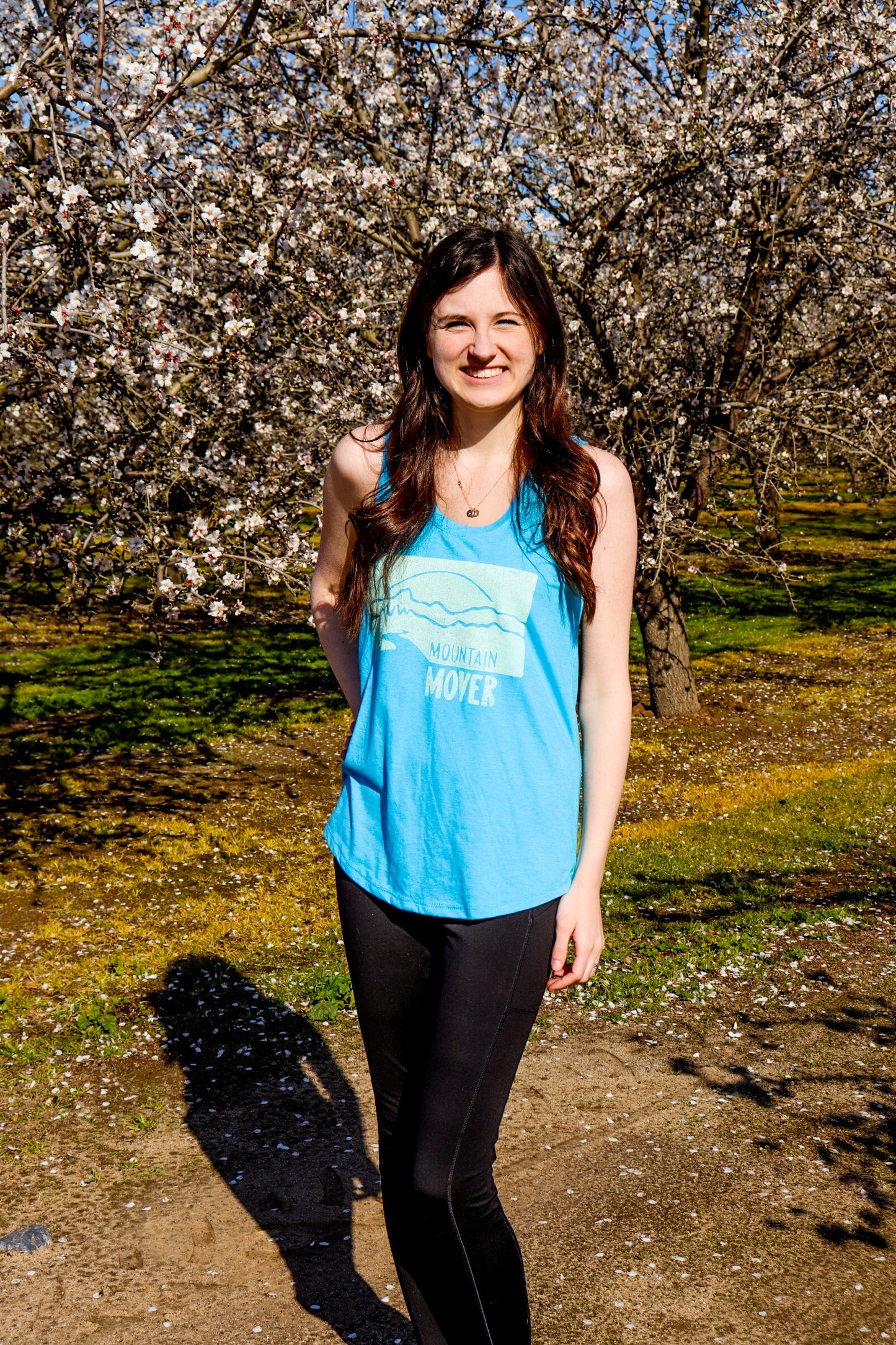 Woman wearing light blue tank top with white mountain mover stamp depicting a mountain scene