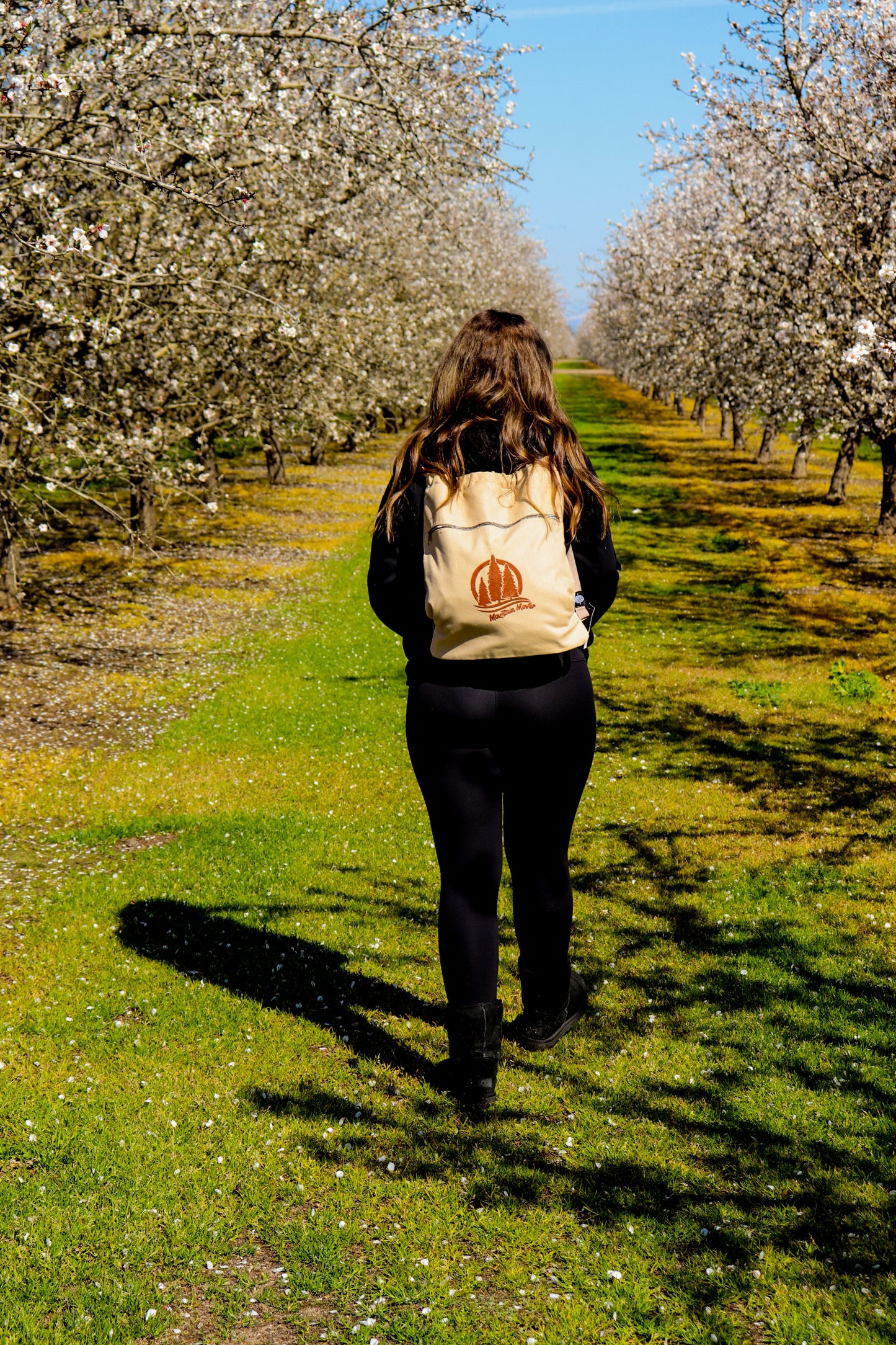 Woman walking with tan drawstring bag on with mountain mover logo stamp
